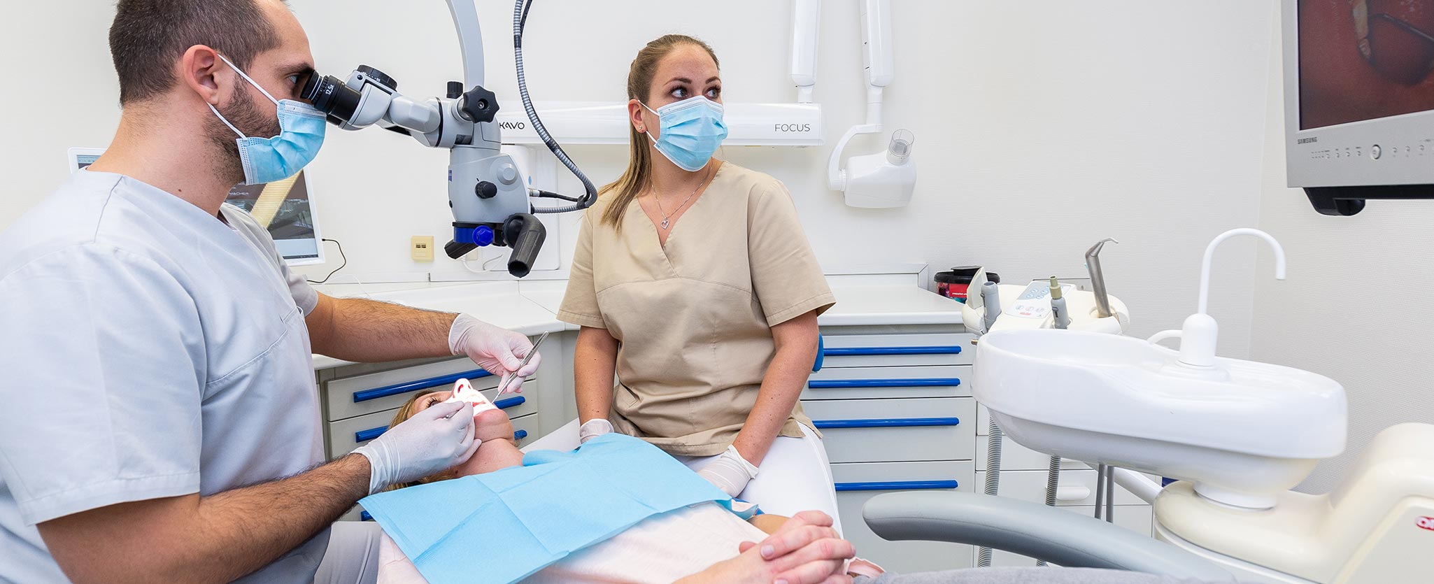 Foto von Zahnarzt Totolici bei der Untersuchung einer Patientin mit dem elektronischen Mikroskop im Behandlungsstuhl, daneben sitzt die Zahnarzthelferin